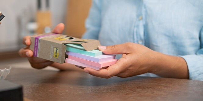 A person taking out a stack of Post-it® Recycled Notes from it’s package.
